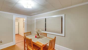 A dining room with a wooden table, four chairs, a vase with dried flowers, and a window with blinds.