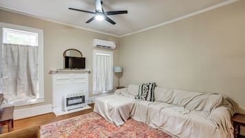 A bedroom with a bed, a ceiling fan, an air conditioning unit, a heater, a window with curtains, and a patterned rug.
