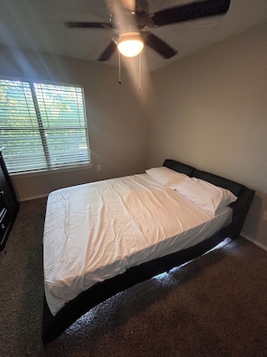 A bedroom with a bed, a ceiling fan, and a window with blinds.
