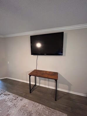 Ein Zimmer mit einem an der Wand befestigten Flachbildfernseher, einer Holzbank und einem gemusterten Teppichboden.