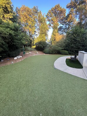 A well-maintained grassy area with a curved concrete path, surrounded by dense shrubbery and trees.