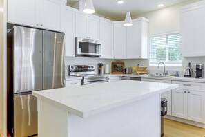 Cozinha moderna com armários brancos, eletrodomésticos de aço inoxidável e iluminação pendente.