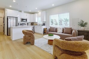 A modern kitchen with white cabinets, stainless steel appliances, and a dining area with a sofa and two woven chairs. - LA Chic: Mid-City Home By Shopping & Hot Spots (Los Angeles)