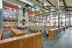 A spacious indoor area with multiple tables and chairs, high ceilings with metal beams, and large windows allowing natural light.
