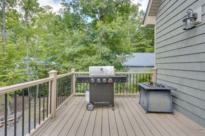 Ein Grill mit Holzkohle auf einer Holzterrasse mit Geländer, ein Gasbehälter und ein kleiner Tisch mit Grillwerkzeug.