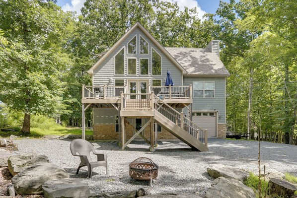 A two-story house with a wooden deck, a stone foundation, and a covered outdoor seating area.