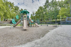 Ein Spielplatz mit Rutschen und Klettergeräten, umgeben von Bäumen und Picknicktischen.
