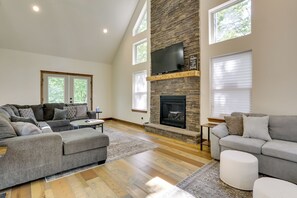 A spacious living room with a stone fireplace, grey sofas, and large windows.