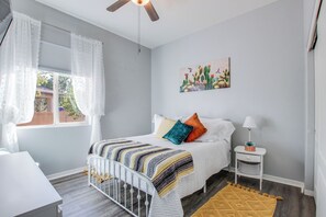 Ein Schlafzimmer mit Bett, Nachttisch, Lampe und einem Fenster mit Vorhängen.
