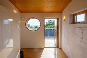 Una habitació amb sostre de fusta, una finestra circular i vista a l'exterior.
