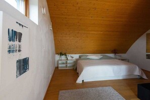 A bedroom with a sloped ceiling, a bed with white bedding, a bedside table with a plant, and a wall with abstract art.