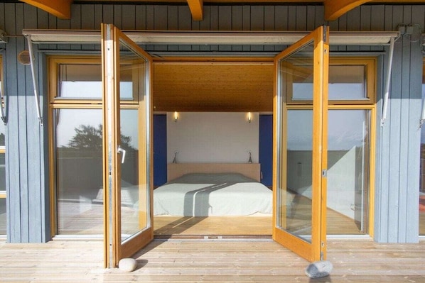 A bedroom with a bed, wooden flooring, and glass doors leading to an outdoor area.