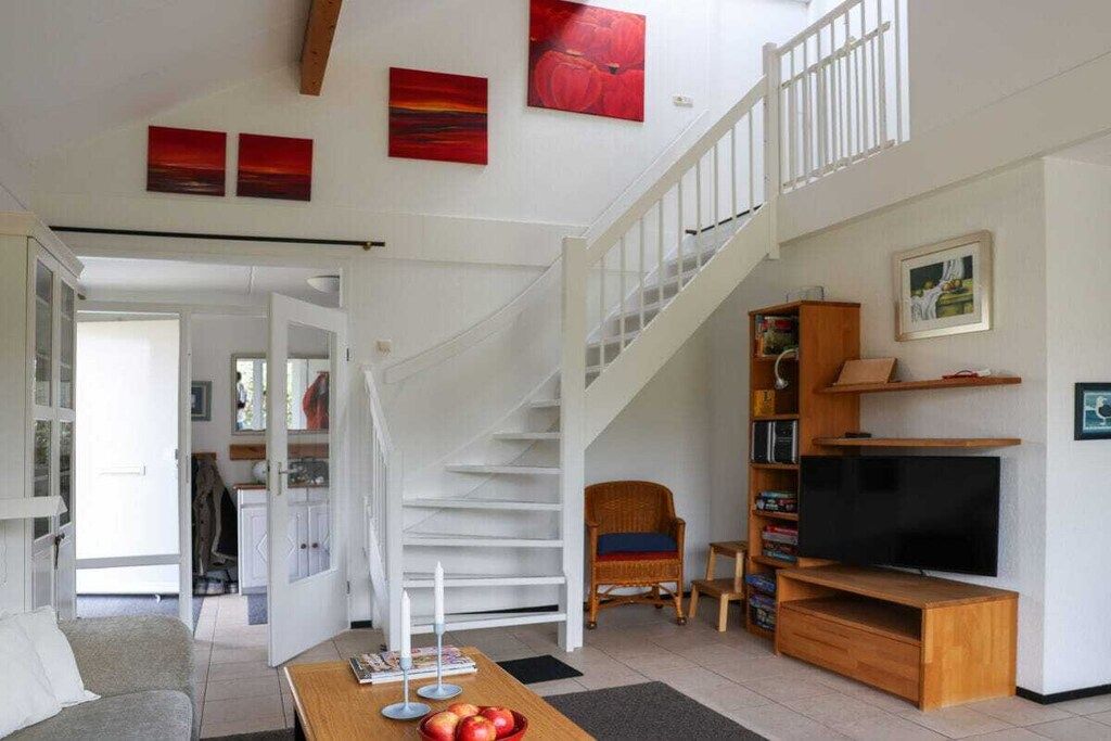 A spacious living area with a staircase, a television, and a bookshelf.