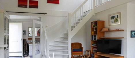 A spacious living area with a staircase, a television, and a bookshelf.
