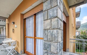 Un balcon avec un mur en pierre, une porte en bois et une table blanche avec des chaises.
