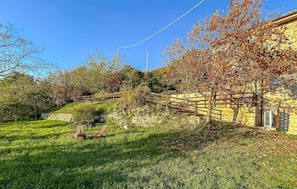 Ett grönområde med en stenmur, ett trästaket och en byggnad med en gul fasad.