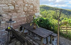 A rustic outdoor seating area with a stone wall, wooden benches, a table with a vase of flowers, and a view of a vineyard. - 3 bedroom lovely home in Cagli (Cagli)