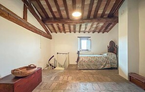 Quarto com teto de madeira, cama com roupa de cama floral, radiador e janela.