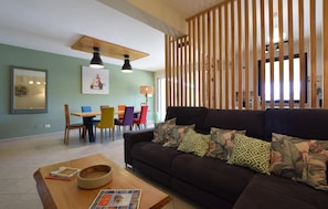 Ein modernes Wohnzimmer mit einem dunklen Sofa, bunten Stühlen, einem Holztisch und einem Essbereich mit Tisch und Stühlen.