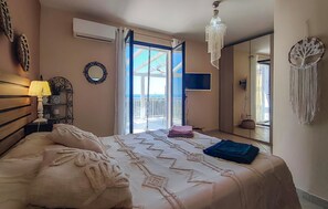Ein Schlafzimmer mit Bett, Nachttischlampe, Spiegel und Blick auf den Balkon.