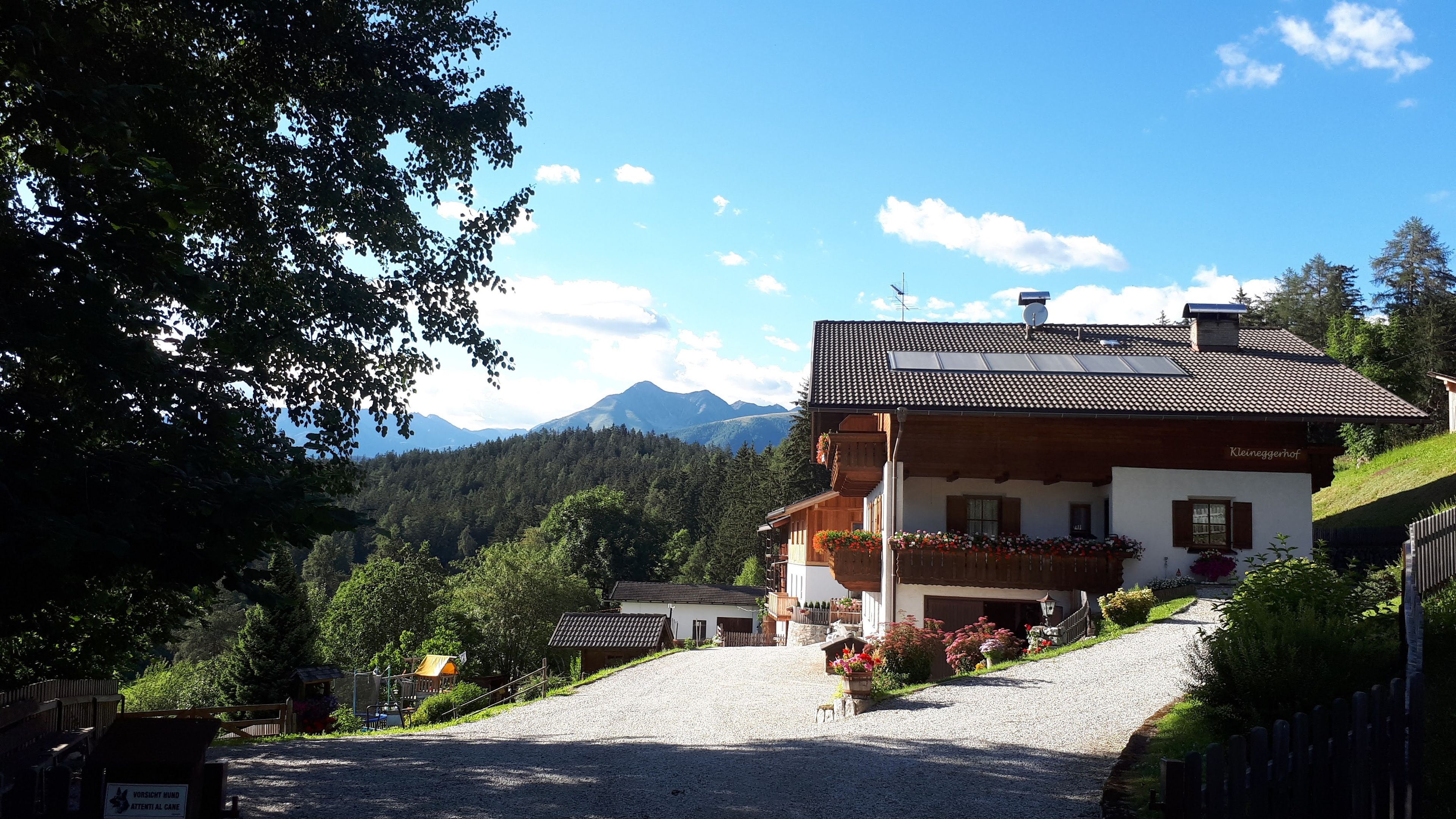Ein traditionelles Chalet mit geneigtem Dach, hölzernen Balkonen und einer Auffahrt mit Kies zum Eingang.