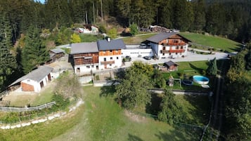 Ein großes Anwesen mit mehreren Gebäuden, darunter ein Haupthaus mit Satteldach, ein Nebengebäude und ein eingezäunter Bereich mit einem Pool.