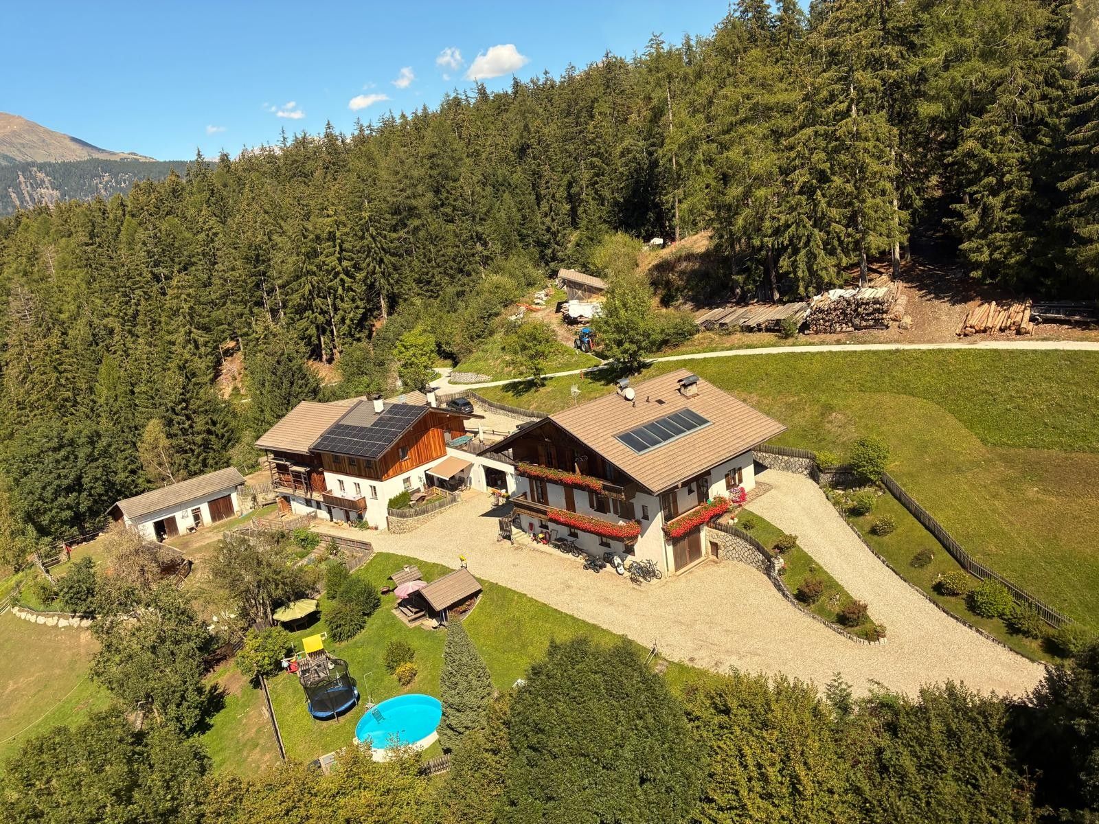 Une grande maison avec une piscine, entourée d’une zone boisée et avec une montagne en arrière-plan.