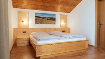 Une chambre avec un plafond en bois, un lit recouvert de draps blancs, une table de chevet et un tableau accroché au mur.