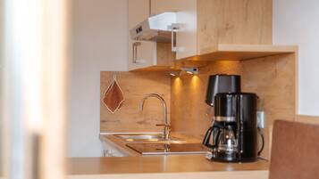 Une cuisine moderne dotée d’un évier en acier inoxydable, d’une machine à café et de meubles de rangement en bois.