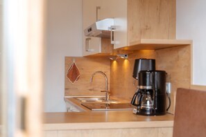 Cozinha moderna com pia de aço inoxidável, cafeteira e armários de madeira.