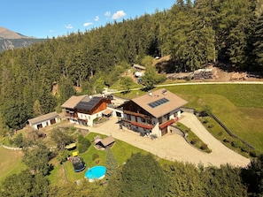 Una casa grande con piscina, rodeada de zona boscosa y una montaña al fondo.
