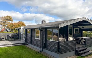 Eine kleine, dunkel gefärbte Holzhütte mit Veranda, Tisch und Stühlen.