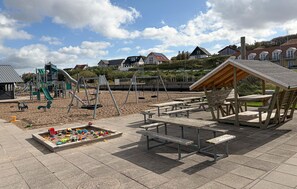 Ein Spielplatz mit Schaukeln, Rutschen, Picknicktischen und einem Sandkasten.