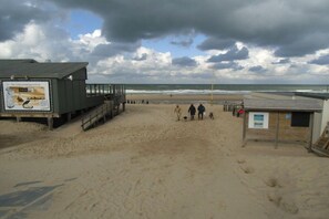 Une plage avec un poste de surveillance pour les sauveteurs, une promenade en bois et un petit bâtiment sur lequel est apposée une enseigne.