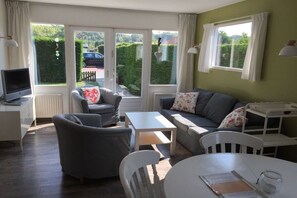Een gemeubileerde woonkamer met een bank, stoelen, een tafel en een televisie.
