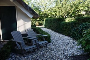A gravel pathway leading to a building with a thatched roof, two Adirondack chairs, and a bird feeder. - Hoeve Duinzicht Burghduin 5 (Burgh-Haamstede)