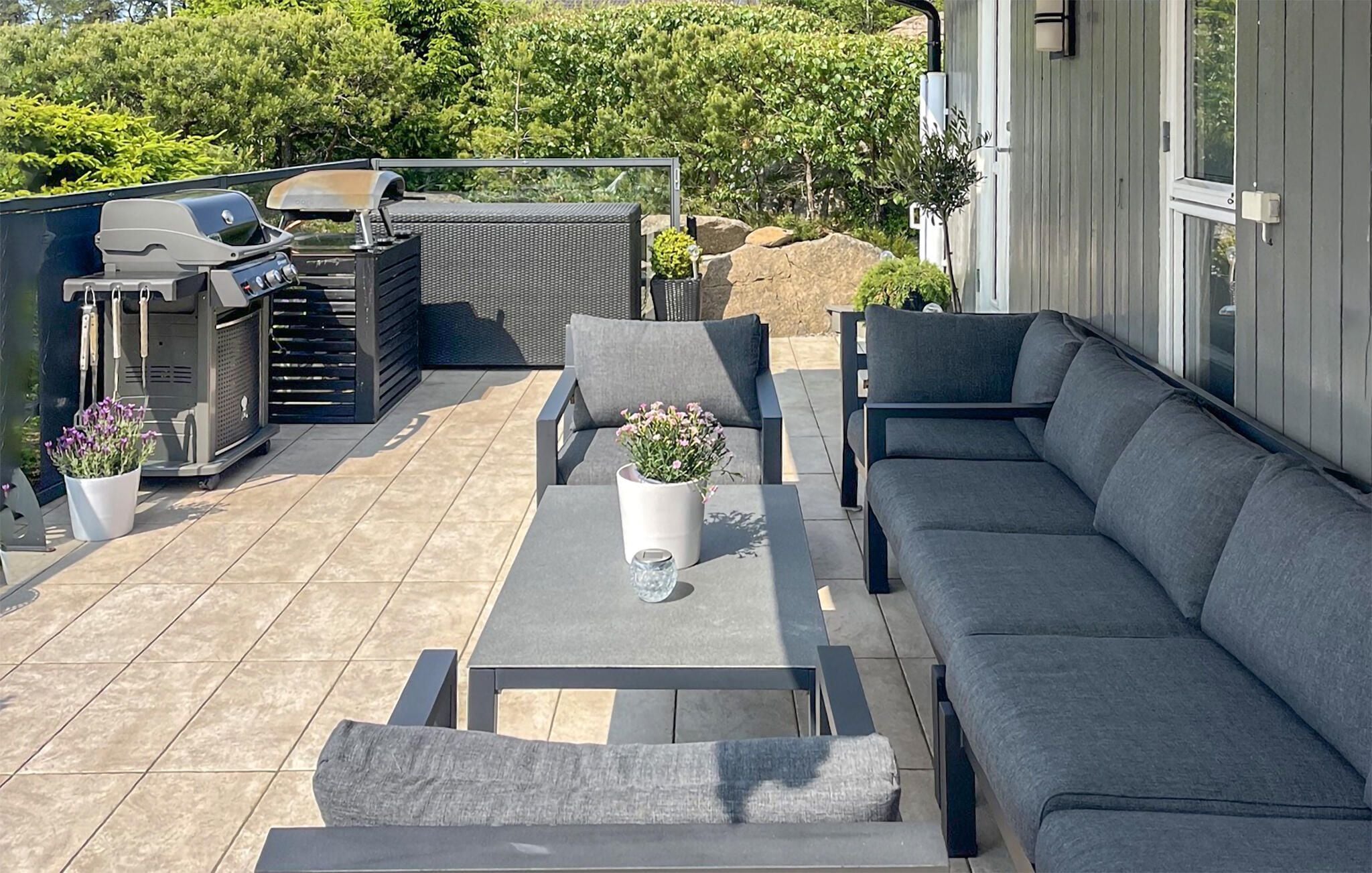 Eine Terrassenausstattung mit Grill, Sitzgelegenheit und Topfpflanzen.
