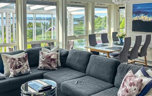 Ein modernes Wohnzimmer mit einem grauen Sofa, einem Glastisch und einem Essbereich mit Tisch und Stühlen.