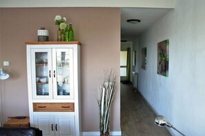 Una sala de estar con un aparador, un jarrón con flores, una lámpara y un pasillo con un cuadro en la pared.