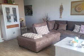 Una sala de estar con un sofá seccional marrón, un aparador blanco y una mesa de centro blanca con objetos decorativos.