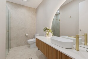 A modern bathroom with a curved vanity, a toilet, and a shower area. - Oceanfront 4-Bed Home Surf & Serenity (Seaford)