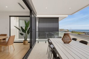 A modern dining area with a view of the sea, a large plant, and a wicker table centerpiece. - Oceanfront 4-Bed Home Surf & Serenity (Seaford)