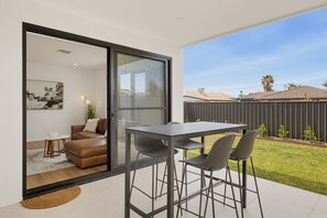 A modern patio with a sliding glass door leading to an interior space, a table with chairs, and a view of a residential area. - Oceanfront 4-Bed Home Surf & Serenity (Seaford)