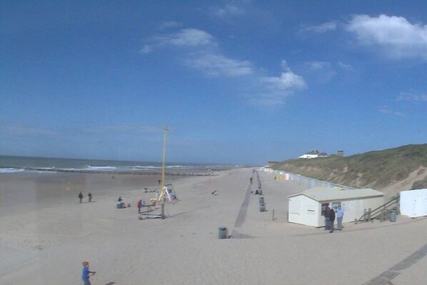 Een strand met een pad dat naar een klein gebouw leidt, mogelijk een post voor strandwachten, en een heuvel met een constructie bovenop.