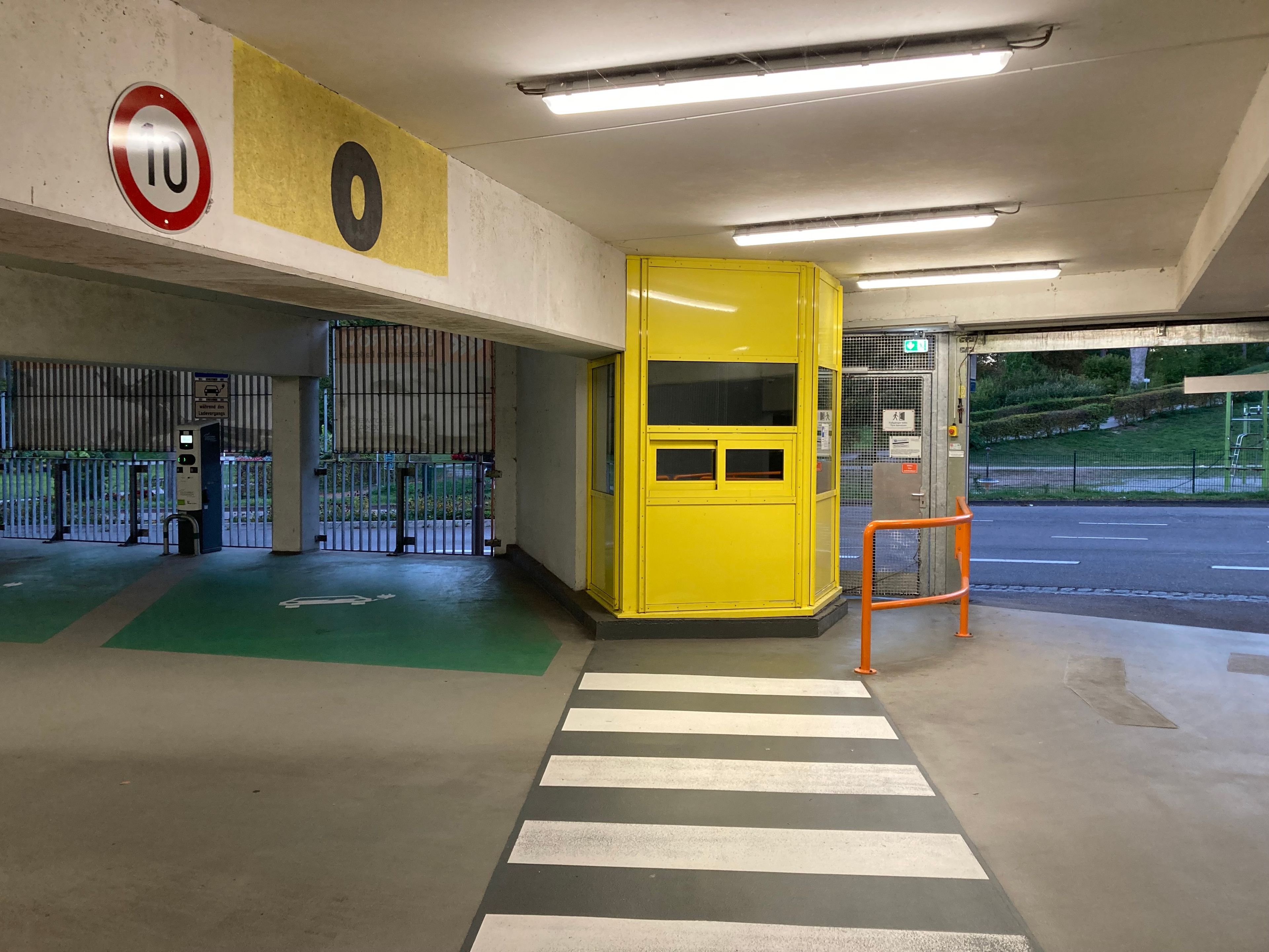 Entrada de un estacionamiento con una puerta amarilla, un cartel de límite de velocidad y un paso de peatones.