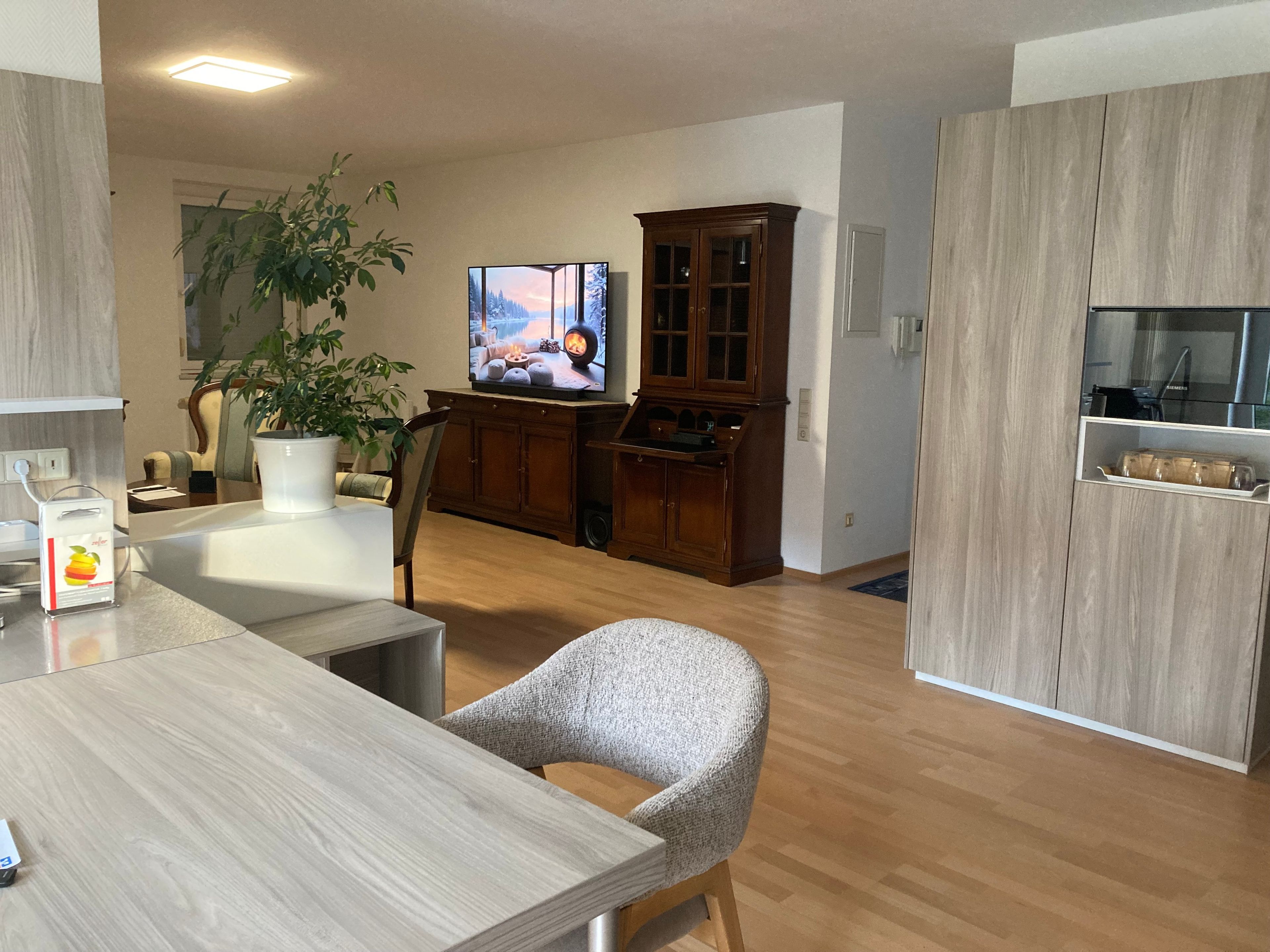 Ein modernes Wohnzimmer mit einem Holzespeisetisch, einem bequemen Sessel, einem Fernseher und einem Schrank.