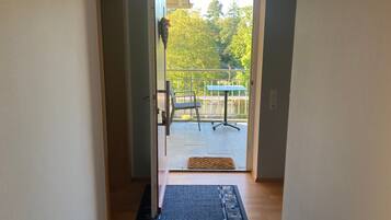 A hallway leading to a balcony with a table and chairs, a doormat, and a view of trees.