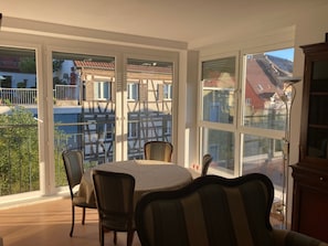 A room with a table and chairs, large windows, and a view of buildings outside. - Apartment 'Fewo Zweischlaf' with Wi-Fi (Stockach)