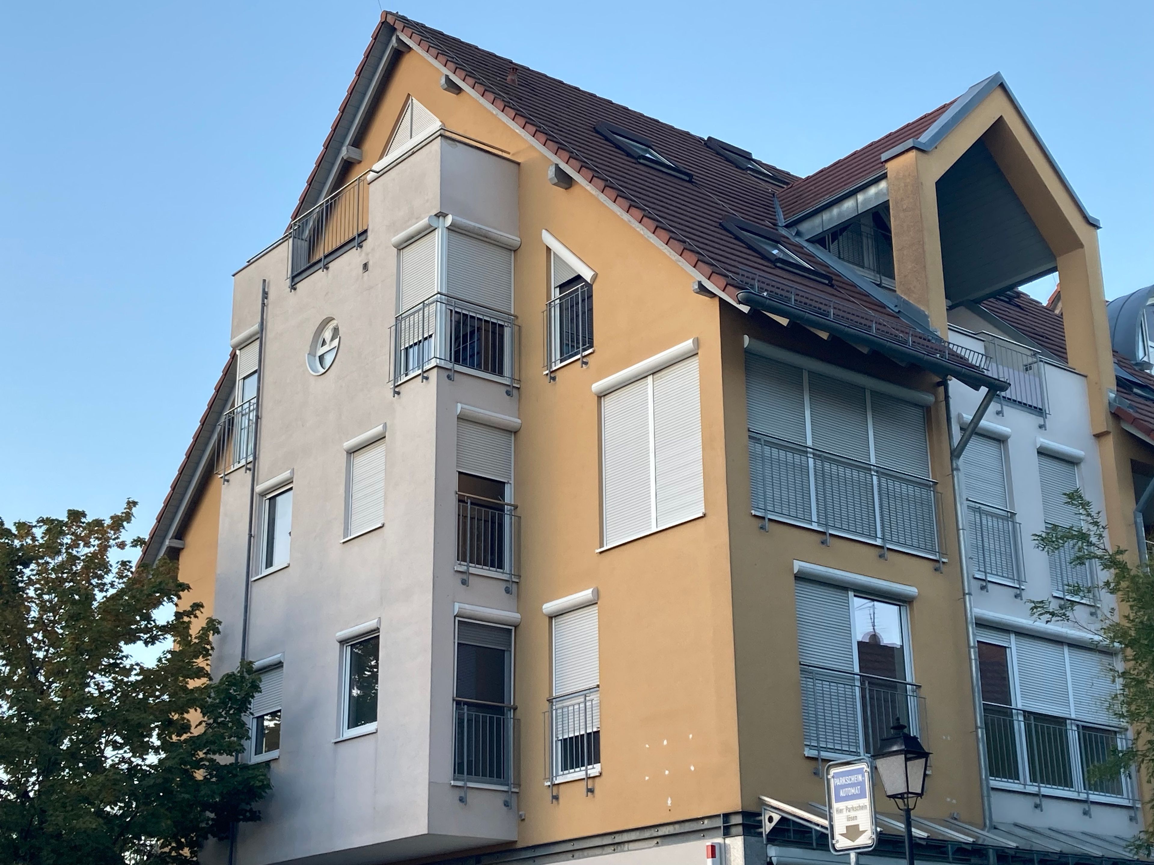 A multi-story building with balconies, windows with shutters, and a sign indicating a parking area.