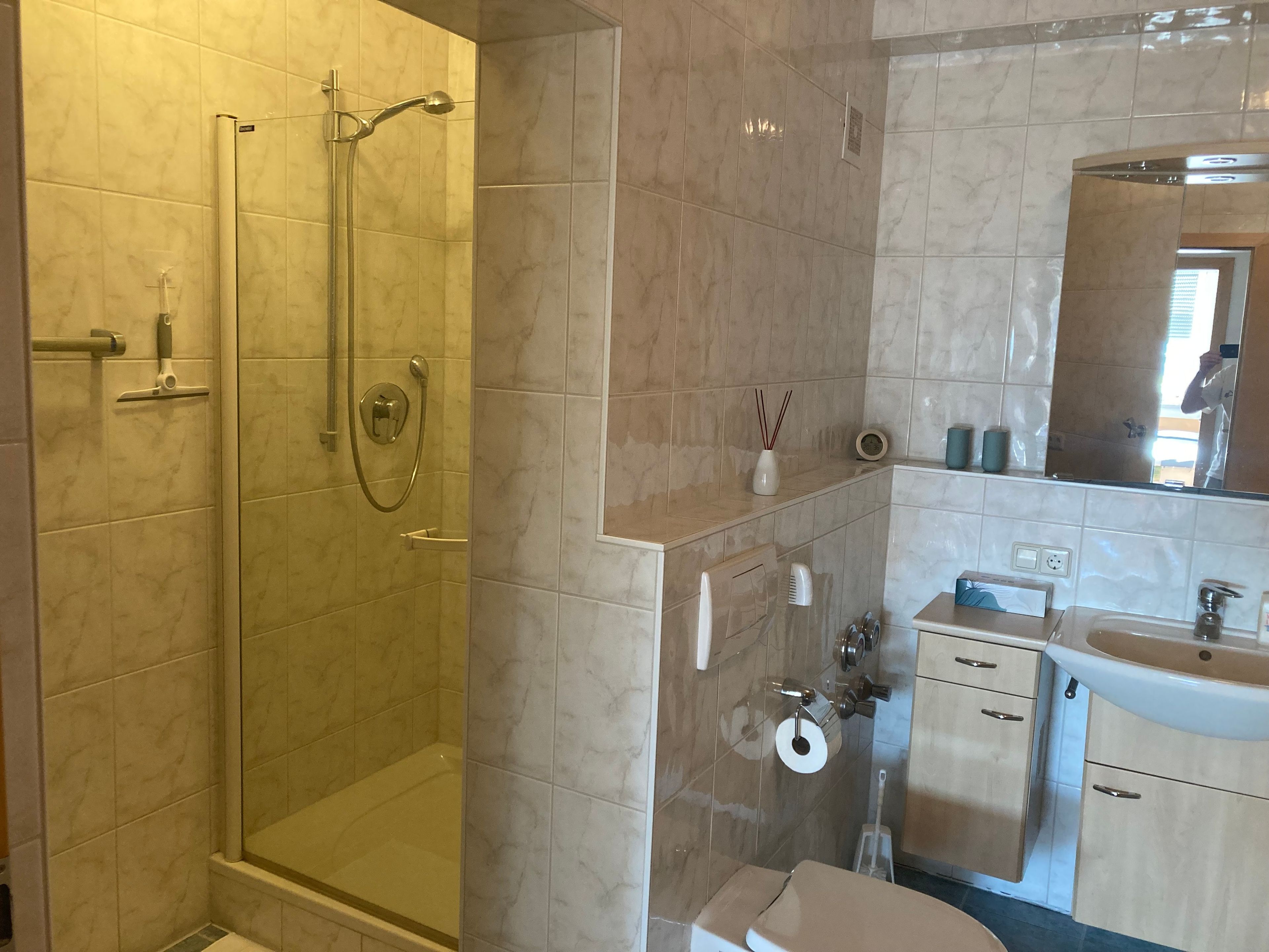Ein Badezimmer mit einer Duschkabine, Toilette, Waschbecken und Spiegel.